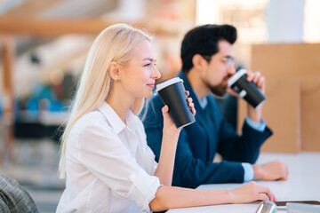 Happy beautiful young young man and woman drinking coffee and resting sitting at table in mall after shopping at mall. Elegance couple relaxing after shopping in cafe, paper bags on table.