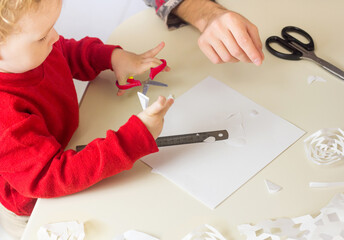Cute little Boy cuts out snowflakes for Christmas decoration. New Year Decor. Festive craft and seasonal activity