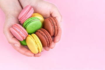 Heap of bright cookies in the hands of a woman on a pink background, copy space.