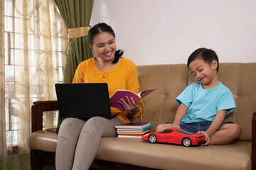 Fototapeta premium A cute Asian boy playing toy cars while accompanying his mother to work