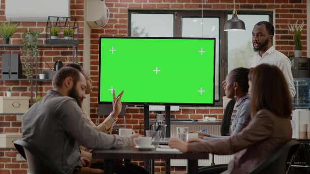 Business man presenting monitor with green screen at meeting with coworkers, looking at mock up background with isolated copy space template. People working with blank chroma key display.