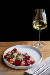 salmon salad with beet cheese and green leaves on wooden table with glass of white wine.
