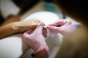 Obraz premium Beauty saloon. Cute Caucasian girl young woman in pink gloves makes manicure client with long hair. Beauty industry, care, profession,