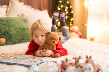 Blond child, toddler boy, having fun at home on Christmas, reading, playing with candy canes