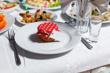 Gift for guests at the wedding on a plate. Bonbonniere in the form of honey in a jar, covered with a red dotted cloth with a bow and nameplate