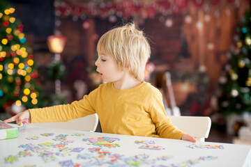 Blond child, toddler boy, having fun at home on Christmas,  assembling puzzle, enjoying