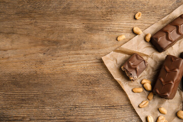 Fototapeta na wymiar Chocolate bars with nuts and parchment on wooden table, flat lay. Space for text