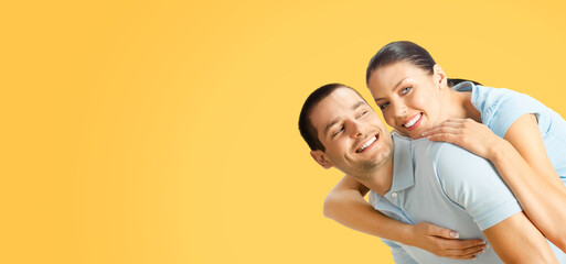 Happy amazed smiling couple. Portrait of excited embracing, piggyback pose models in love studio concept, over yellow color background. Brunette man and woman. Copy space area.