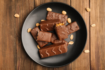 Plate of chocolate bars with caramel, nuts and nougat on wooden table, top view