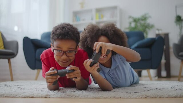 Two active african american kids playing video game on floor having fun together
