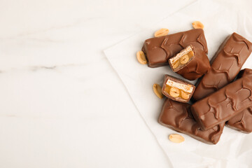 Chocolate bars with caramel, nuts and nougat on white marble table, flat lay. space for text