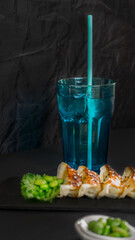 A blue glass of drink and gyoza on a black background, asian food