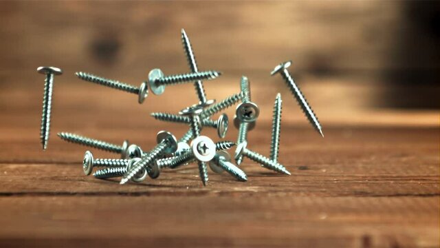 Screws fall on the table. On a wooden background. Filmed is slow motion 1000 frames per second. High quality FullHD footage