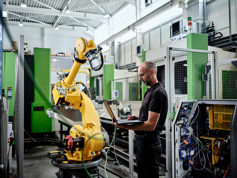 Male engineer using laptop by robotic arm