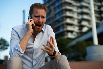 Businessman using the phone while sitting on the stairs. Angry upset man using the phone.