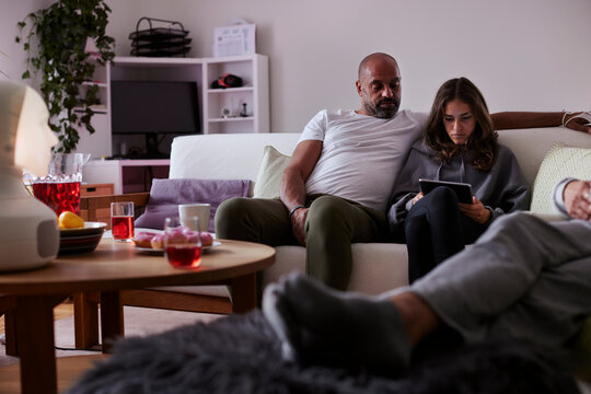 Father and daughter sitting on sofa and using tablet
