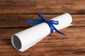 Rolled student's diploma with blue ribbon on wooden table - obrazy, fototapety, plakaty