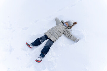 Fototapeta na wymiar Cheerful children lying in the snow. Happy kid making snow angel. Kids play outside in winter