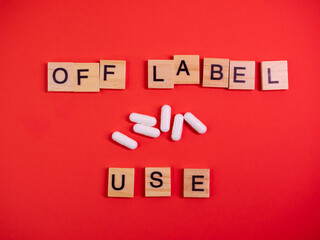 Off label approved medicine pill use. Covid-19 therapy. Words off label and white capsules or pill drugs on colored red paper texture background. Pharmacy concept. Copy space. Mock up design template