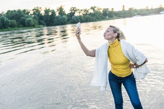 Woman puckering while taking selfie through smart phone at riverbank