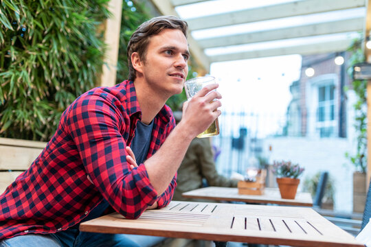 Man looking away while sitting at table holding beer glass