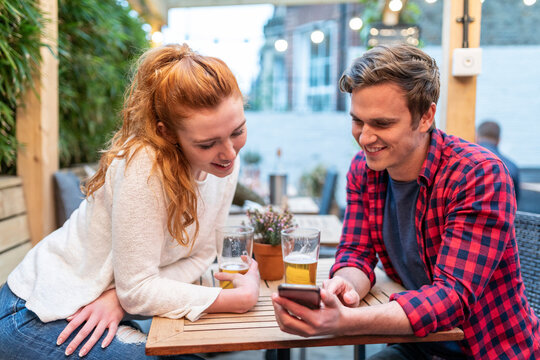 Couple looking at smart phone while having beer at pub