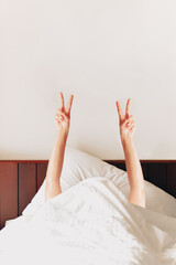 Woman showing victory sign with fingers while lying on bed in morning.