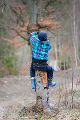 Boy climbing on a cut trunk. Kid having fun outside on a grey, winter, cold day