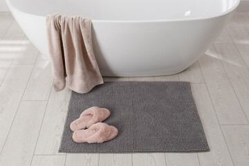 Soft grey bath mat and slippers on floor in bathroom - obrazy, fototapety, plakaty