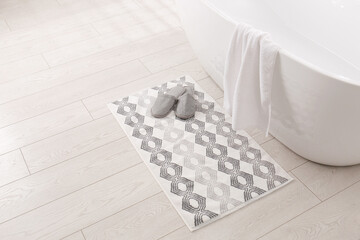 Soft bath mat and slippers on floor in bathroom
