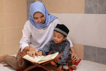 an Asian mother is teaching her son to read Al-Qur'an