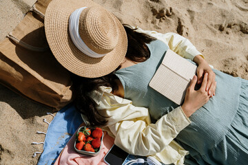 Woman covering face with hat while lying on beach