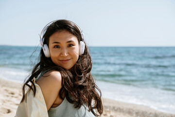 Beautiful woman wearing headphones smiling at beach on sunny day