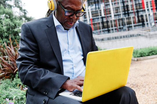 Male professional with headphones using laptop while sitting at garden