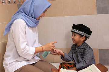 a Muslim Asian mother is wearing a sanitizer to her son who is reading the Al-Qur'an