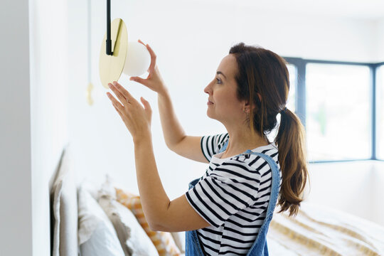 Mid adult woman installing bulb in bedroom while relocation in new home