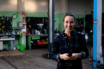 Smiling female mechanic with equipment standing at repair shop