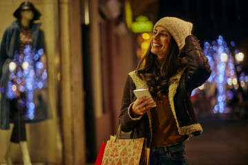 Pretty young woman with mobile phone by the shop window at Christmas time