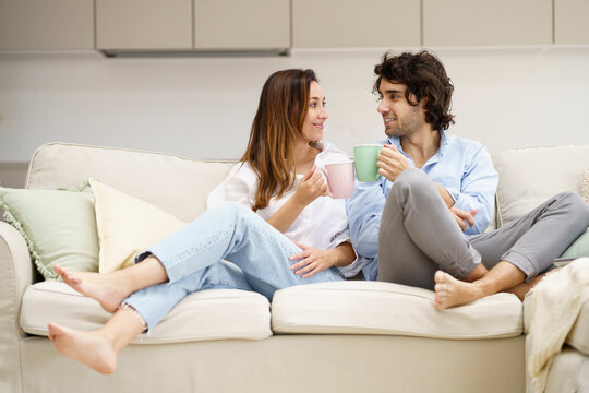 Smiling couple having coffee while sitting on sofa at new home