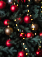 Blurred background of dressed up Christmas tree. Close-up of green branches of a Christmas tree with New Year's toys: red and gold balls. Christmas tree garland. Christmas. New Year.