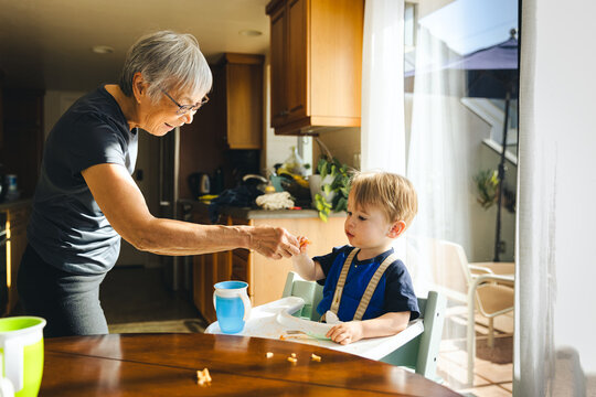 Grandmother Giving Food To Grandson At Home