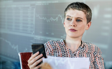 Female professional holding smart phone while looking at graph on digital wall