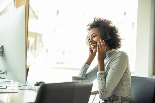 Smiling businesswoman holding headset while looking at computer in office