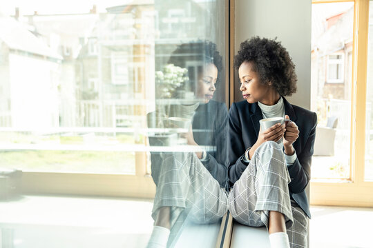 Female professional looking down while sitting on window sill at office
