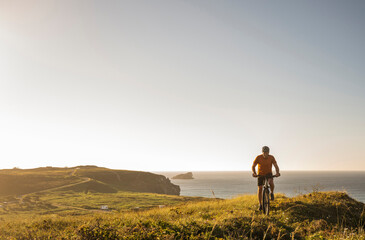 Male athlete riding bicycle on green landscape by sea