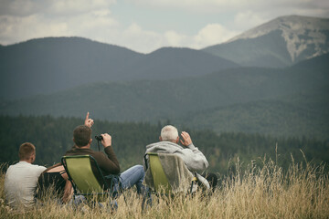A family of different generations sits with their backs in armchairs and looks at the mountains.