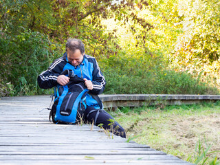 Fototapeta premium Man sitting on wooden path, middle age tourist enjoying sunny day in autumn nature