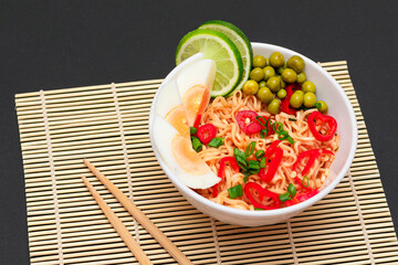 Beautiful Noodle Dish with Green Pea, Eggs, Red Hot Pepper, Greens and Lime with Chopsticks on Sushi Mat. Instant Noodles