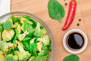 Fresh Green Salad of Avocado, Broccoli, Spinach and Cucumber with Soy Sauce and Red Hot Pepper on Wooden Cutting Board. Vegan Salad. Vegetarian Culture. Raw Food. Healthy Eating and Vegetable Diet