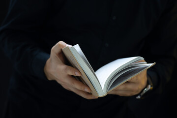 the hands of a man in black clothes who holds a book and tries to open it